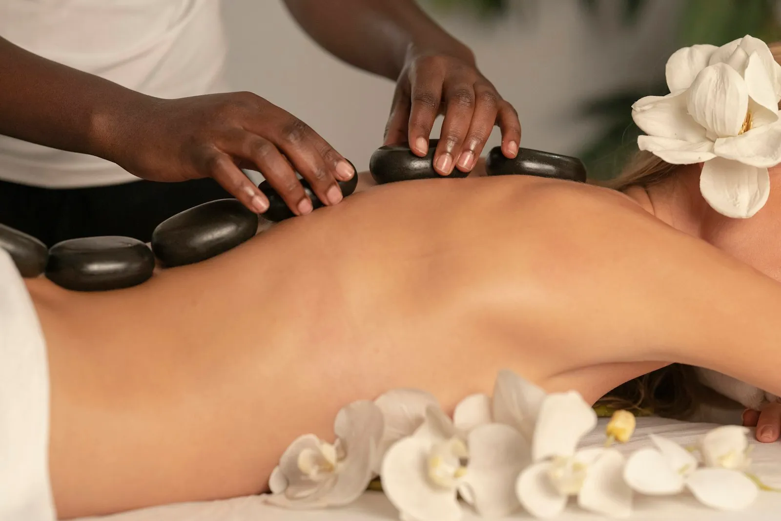Massage table dressed in white linen, neutral wood walls in the background.